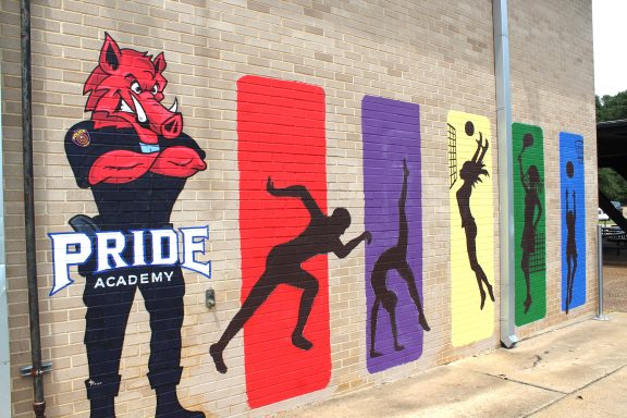 Mural of "Pride Academy" and icons on wall of school building