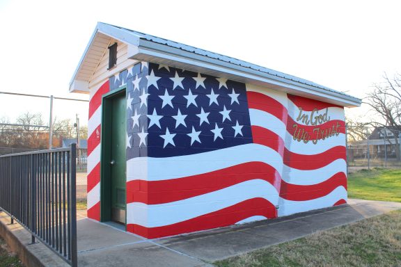 Mural of U.S.A. Banner painted on sides of a small building in a park.