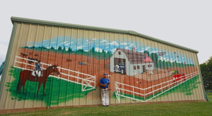 Chris Opp standing in front of mural of a farm painted on a building