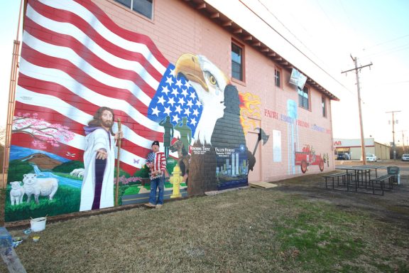Mural on the side of a building with U. S. A. Banner, Jesus, eagle, firefighter and more