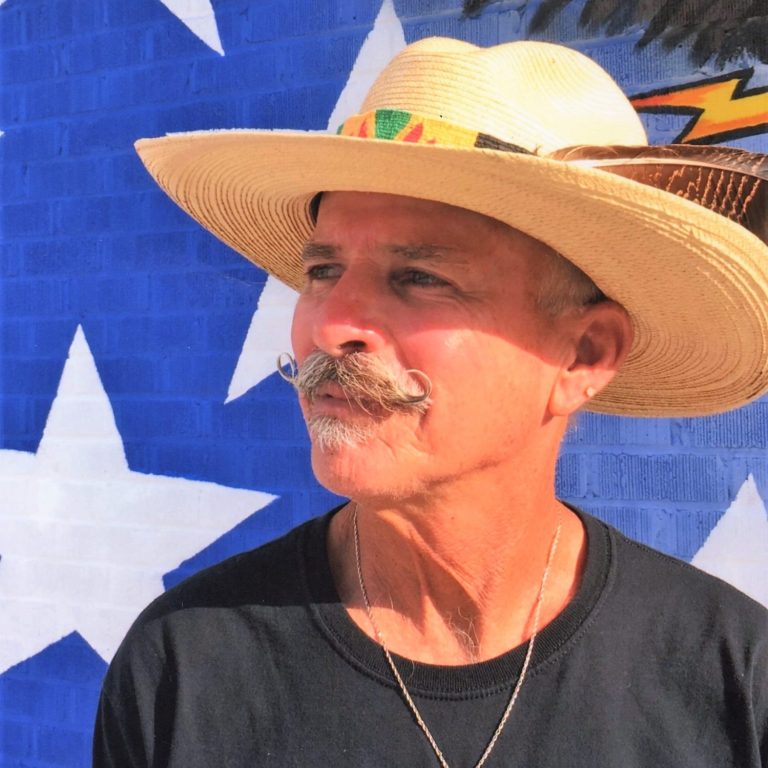Chris Opp, has light complexion, mustache, wearing a straw hat with a feather.