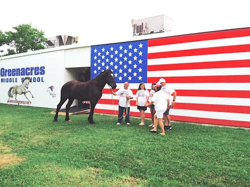 Group of people with a horse standing in front of the U. S. A. Banner