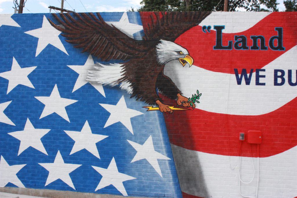 Eagle clutching lightning bolt in one claw, flying over an American Banner