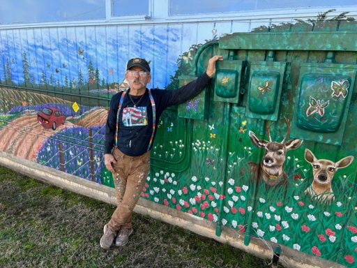 Chris Opp standing next to mural he painted of country scene on a fence
